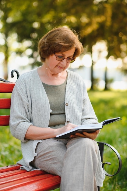 Elegante oudere vrouw in het shirt zit op een warme dag op de bank in een park