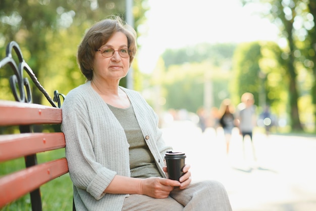 Elegante oudere vrouw in het shirt zit op een warme dag op de bank in een park