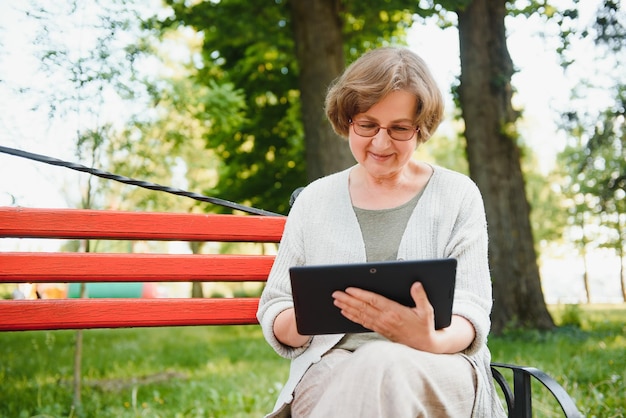 Elegante oudere vrouw in het shirt zit op een warme dag op de bank in een park