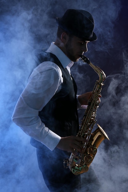 Foto elegante saxofonist speelt jazz op donkere achtergrond in blauwe rook