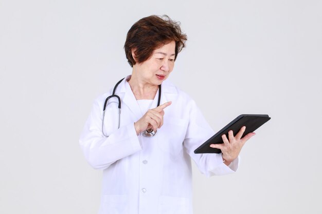 Elegante senior vrouwelijke arts op doktersjurk die vol vertrouwen staat als ziekenhuisgezondheidsdeskundige voor ziektebehandeling in de kliniek.
