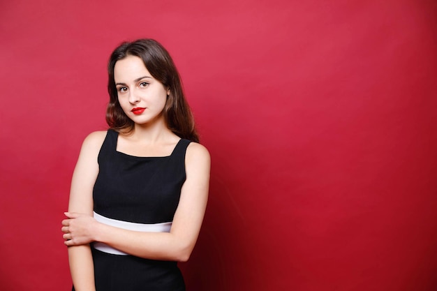 Elegante serieuze vrouw met felle lippenstift in zwarte jurk die staat en naar de camera kijkt op rode achtergrond zwarte vrijdag concept