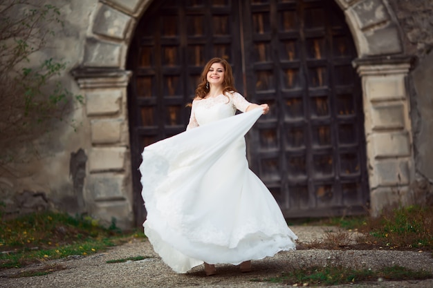 Elegante stijlvolle lieve jonge mooie gelukkige bruid in geweldige trouwjurk staat op het oude paleis. Trouwdag