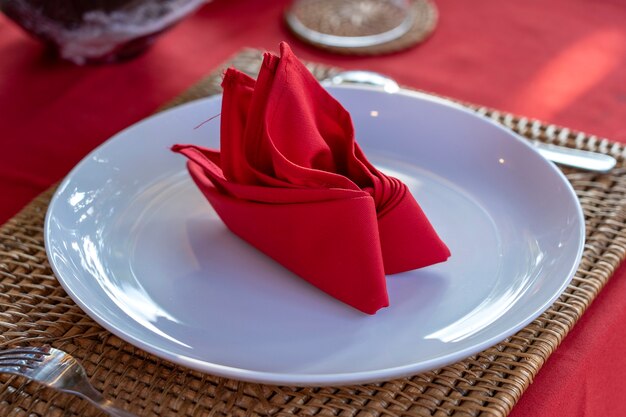 Elegante tafel setting met vork, lepel, witte plaat en rood servet in restaurant, close-up. Leuke eettafel set met gearrangeerd bestek en servetten