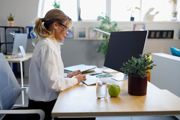 Foto elegante volwassen zakenvrouw die op de computer op kantoor werkt