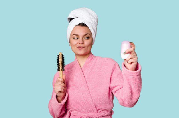 Elegante vrouw in een roze badjas klaar voor de dag met een haarborstel en deodorant in de hand