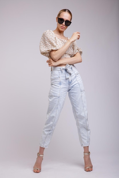 elegante vrouw in mooie blauwe denim jeans, beige top, zonnebril op witte achtergrond