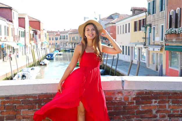 Elegante vrouw in rode lange jurk lopen op brug in het oude centrum van murano, venetië, italië