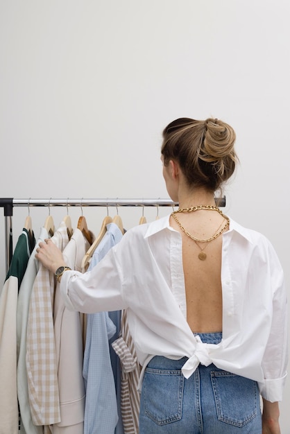 Elegante vrouw terug naar camera in de buurt van minimalistisch kledingrek