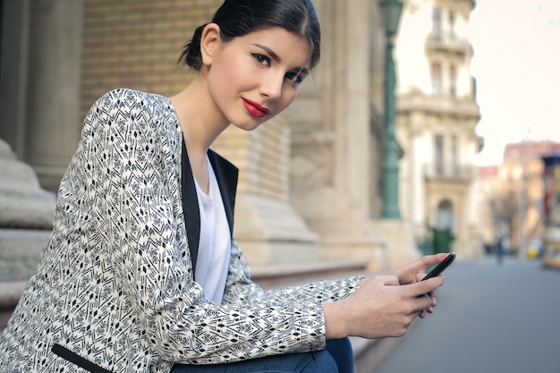 Elegante vrouw zittend op een trap en een smartphone te houden