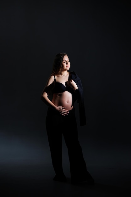 Elegante zwangere vrouw Mooi zwanger meisje met lang haar in zwart pak op grijze achtergrond concept van gelukkige zwangerschap en familie
