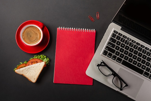 Elegante zwarte office-desktop met laptop, kopje koffie en een broodje voor de lunch. Bovenaanzicht met kopie ruimte.