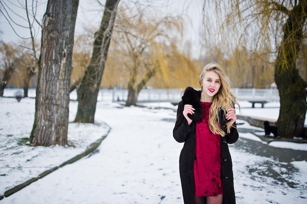 Elegantie blond meisje in bontjas en rode avondjurk geposeerd op besneeuwde winterdag