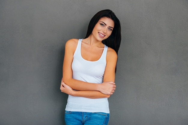 Elegantie en schoonheid. Mooie jonge vrouw in witte tanktop die de armen gekruist houdt en glimlacht