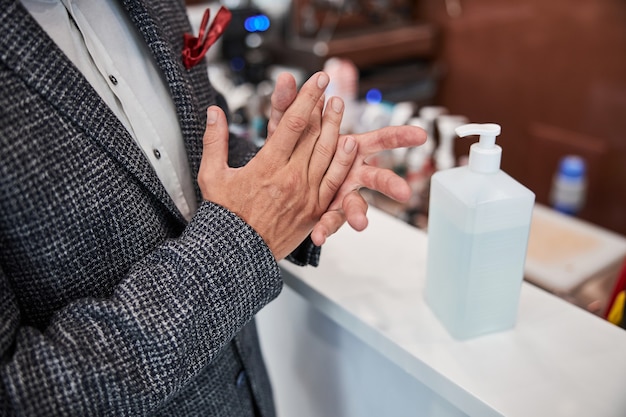 an elegantly-dressed man rubbing sanitizer from a big bottle on his hands