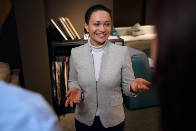 Elegantly dressed woman interior designer smiling toothy smile while serving clients and helping to choose upholstery for new home design project in furniture store