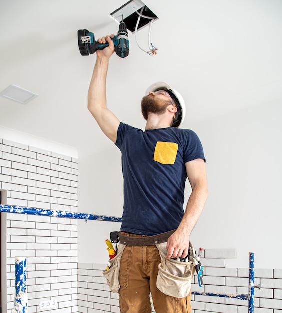 Elektricien bouwer aan het werk, installatie van lampen op hoogte. professioneel in overall met een boormachine op de reparatielocatie.