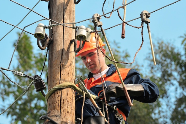 Elektricien op een houten pyloon installeert de aarding op de hoogspanningslijn voordat deze wordt gerepareerd.