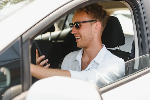 Elektrische autobestuurder - groene energie biobrandstof concept. Man achter het stuur. Man rijdt nieuw milieuvriendelijk voertuig Jonge mannelijke eigenaar trots zelfverzekerd kijken naar camera, taxichauffeur concept.