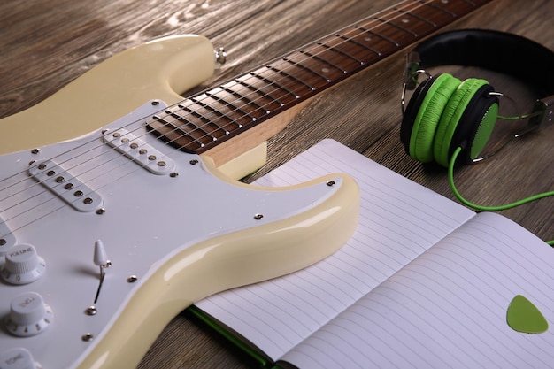 Foto elektrische gitaar met groene koptelefoon en notitieboek op houten achtergrond