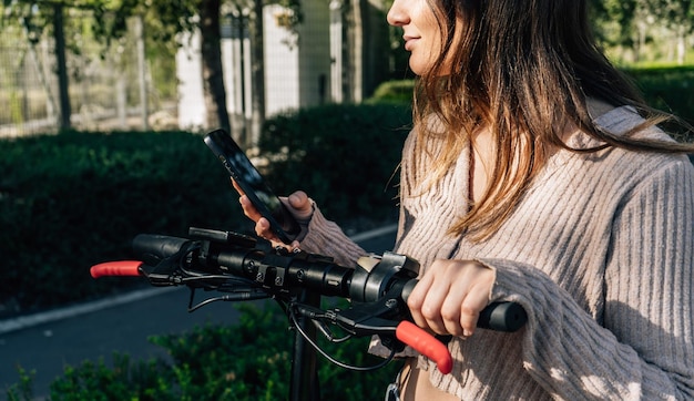 Foto elektrische scooter en mobiel apparaat meisje gebruikt haar telefoon om een elektrische patina bijgesneden opname te ontgrendelen