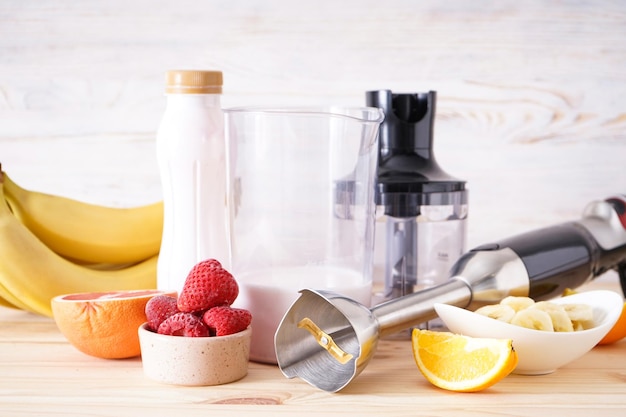 Elektrische staafmixer met gesneden fruit op houten ondergrond.