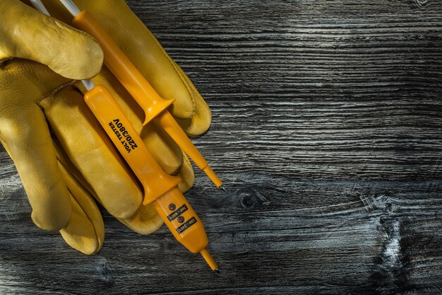 Elektrische tester lederen beschermende handschoenen op vintage houten plank