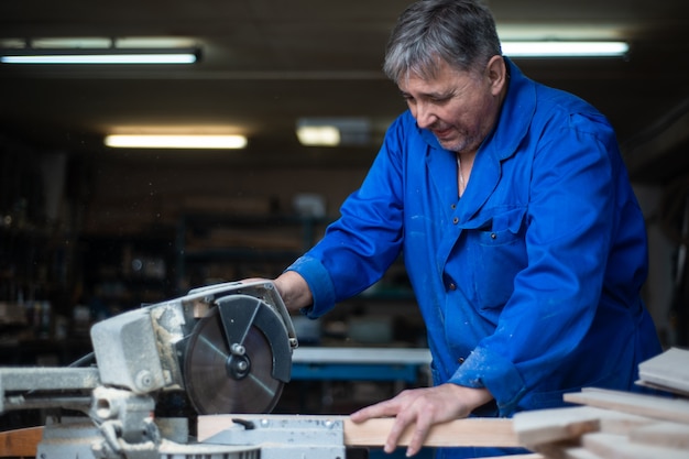 Elektrische zaag voor het zagen van planken, de werknemer zaagt een houten plank in de werkplaats