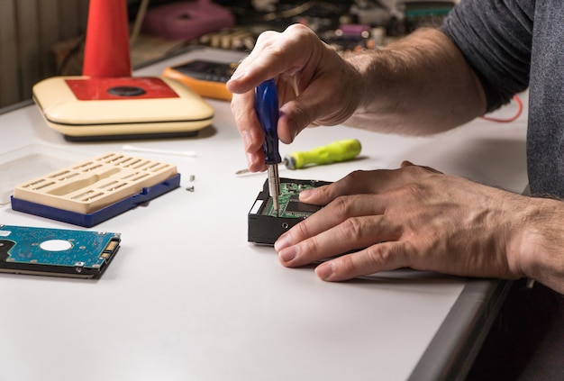 Elektronisch ingenieur repareert de harde schijf van de computer. technoloog met een schroevendraaier demonteert hdd