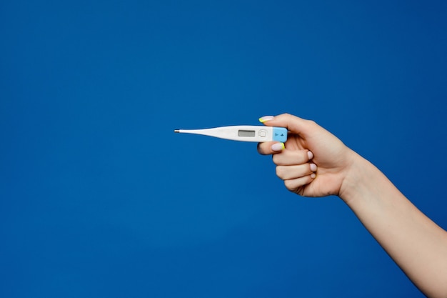 Elektronische medische thermometer in een nette vrouwelijke hand met manicure geïsoleerd op een blauw met kopie ruimte. Medisch hulpmiddel in het seizoen van griep, epidemie en ziekte. Geneeskunde advertentie schot