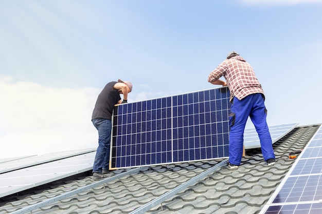 Elektrotechnici werken aan het installeren van zonnepanelen op het zonnestation op het dak van het huis tegen de blauwe lucht