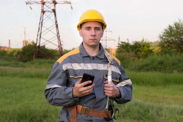 Elektrotechnisch ingenieur in beschermende kleding met een mobiele telefoon in zijn handen