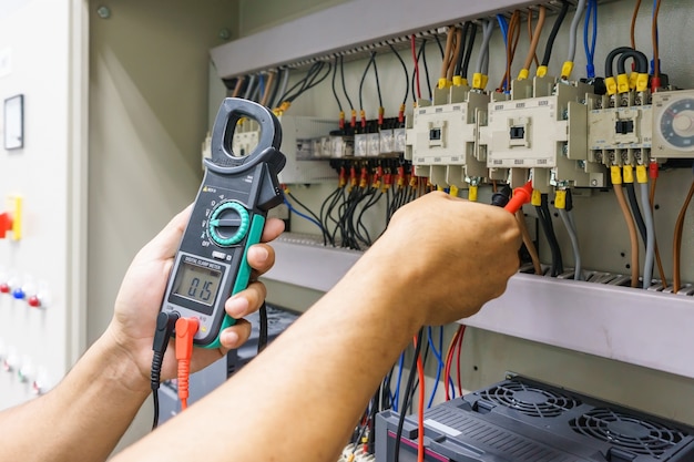 Elektrotechnisch ingenieur past elektrische apparatuur aan met een multimetertester in zijn hand