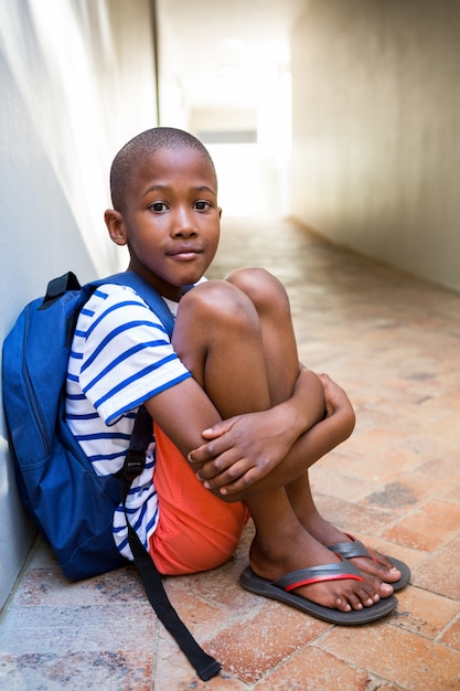 Elementary boy sitting on corridor in school