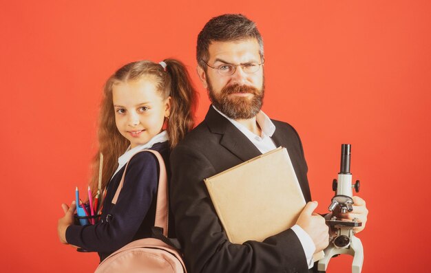 Allievo elementare con insegnante in studio rosso isolato ritratto di ragazza divertente scuola e tutor con materiale scolastico felice insegnante e studente ragazza sul rosso