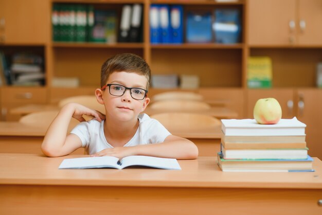 学業の新しいアイデアを見つけようとしている教室の机の小学生の男の子。