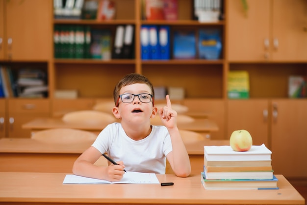 学業の新しいアイデアを見つけようとしている教室の机の小学生の男の子。