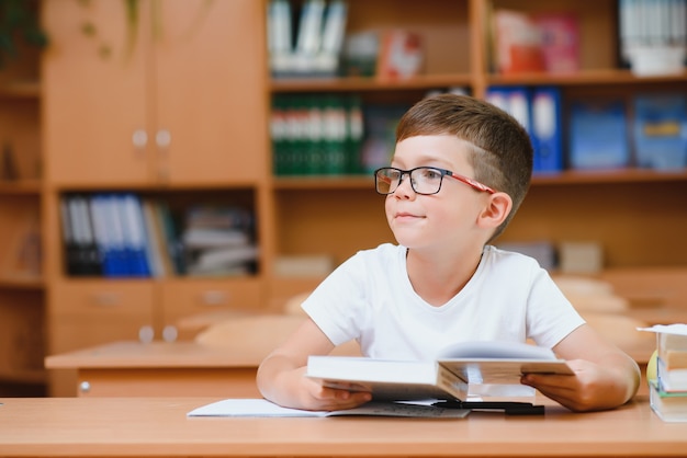 学業の新しいアイデアを見つけようとしている教室の机の小学生の男の子。