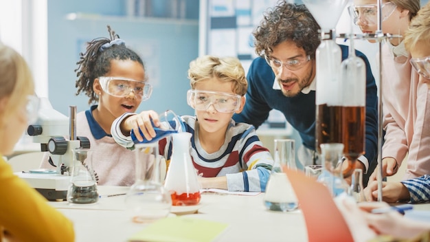 Photo elementary school science classroom little boy mixes chemicals in beakers enthusiastic teacher explains chemistry to diverse group of children children learn with interest