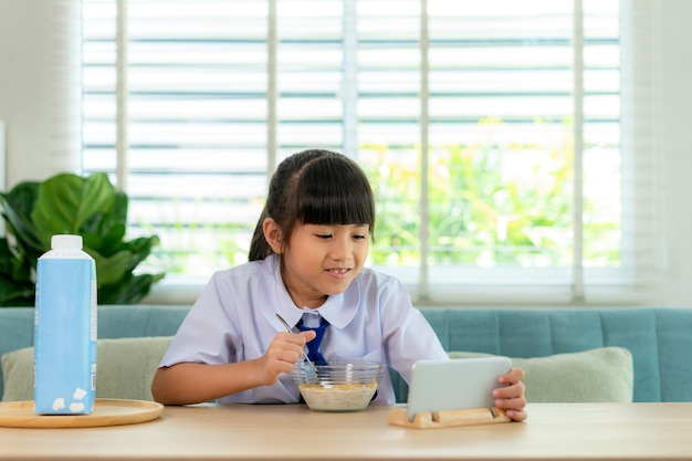 Elementary school student girl in uniform eating breakfast cereals with milk