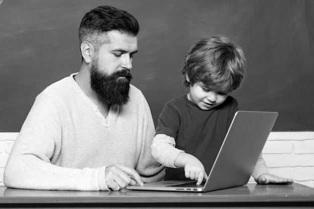 Elementary school teacher and student in classroom teacher and schoolboy using laptop in class chalk