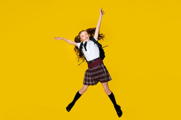 Elementary schoolgirl jumping on yellow background