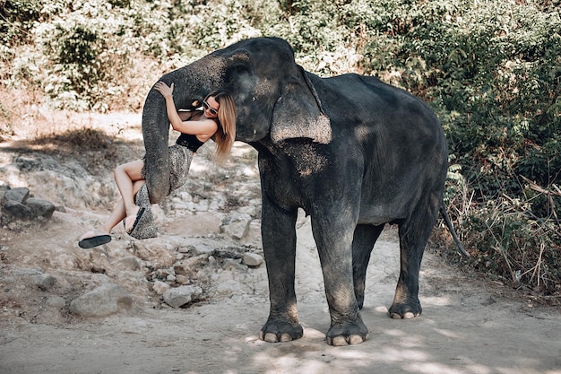 Elephant lifts a beautiful woman in dress with leopard print with its trunk; zoo, Thailand.