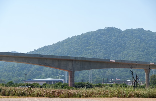 The elevated railway of the double-track project is under construction near the mountain,  along the corn farm to the small town in the valley, front view for the copy space.