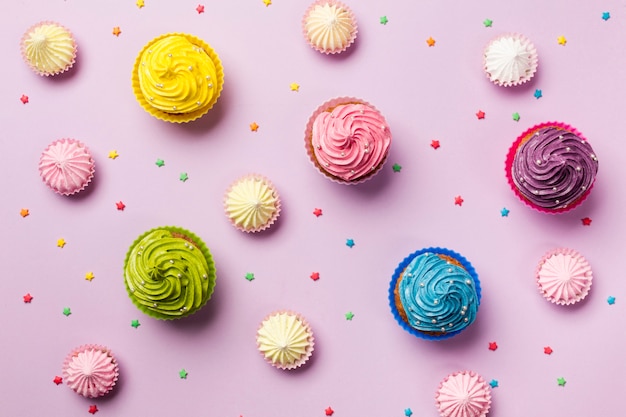 An elevated view of colorful star sprinkles; aalaw and muffins on pink background