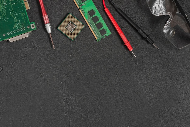 Photo elevated view of computer parts; safety glasses and digital multimeter on black backdrop