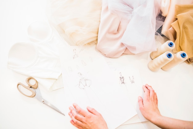 Photo elevated view of designer's hand with fashion sketch and fabric on workdesk