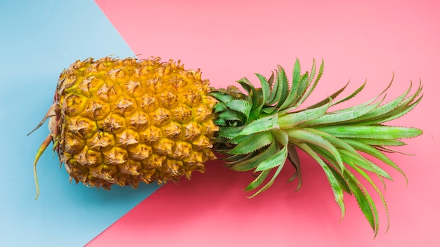 Elevated view of pineapple and blue cardboard paper on pink background