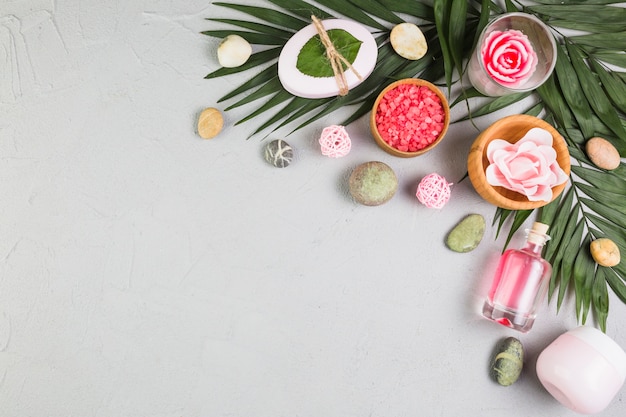 Photo elevated view of soap; spa stones; leaves; moisturizing cream; oil and flowers on grey surface