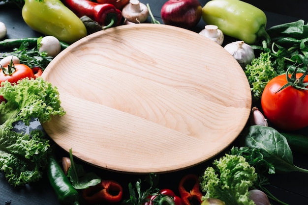 Photo elevated view of wooden tray surrounded with raw vegetables